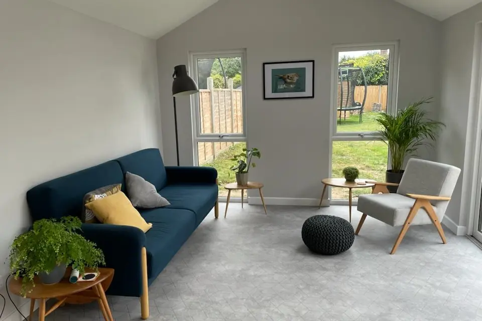 Bright furnished garden-room interior with a blue sofa, armchair and garden-facing windows