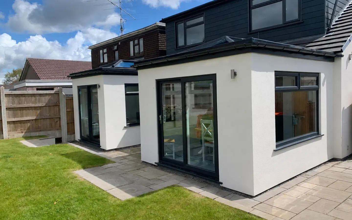 White rendered modular extension with dark-framed doors and windows opening onto a paved garden